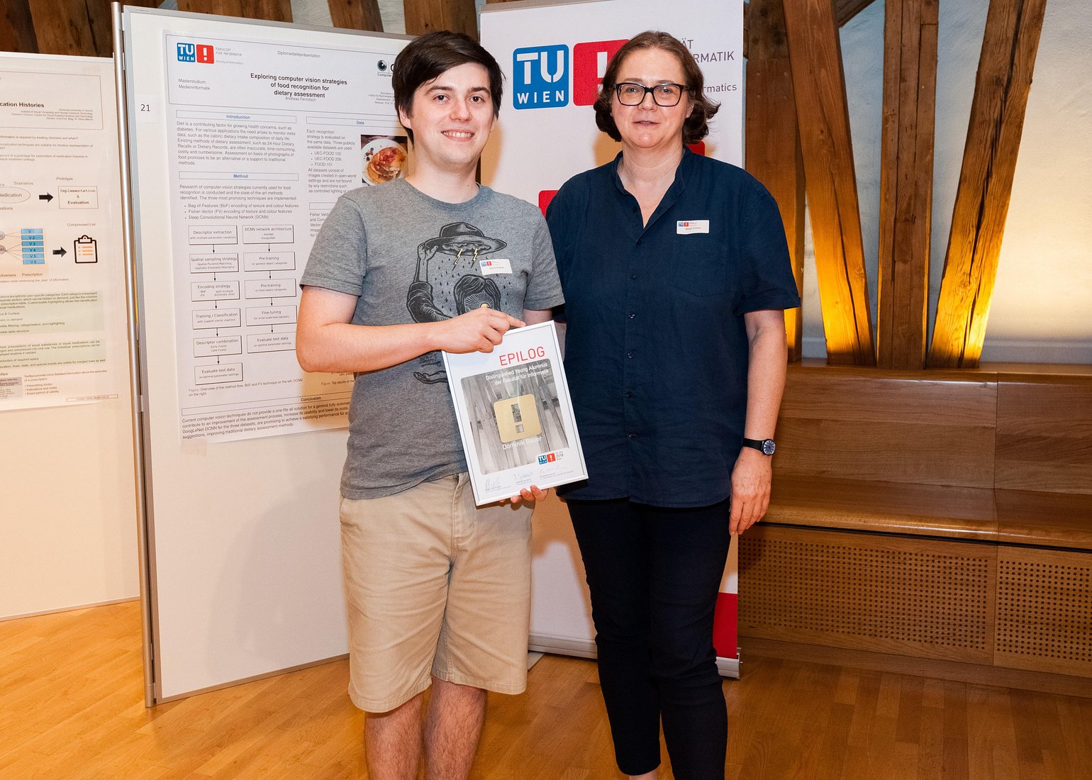 Prof. Dr. Margrit Gelautz, Vorsitzende der EPILOG-Jury, übergibt den Hauptpreis an Dominik Bauer für seine Diplomarbeit "Evaluation of the Recognition Distances of Safety Signs in VR Considering Vision Impairments"