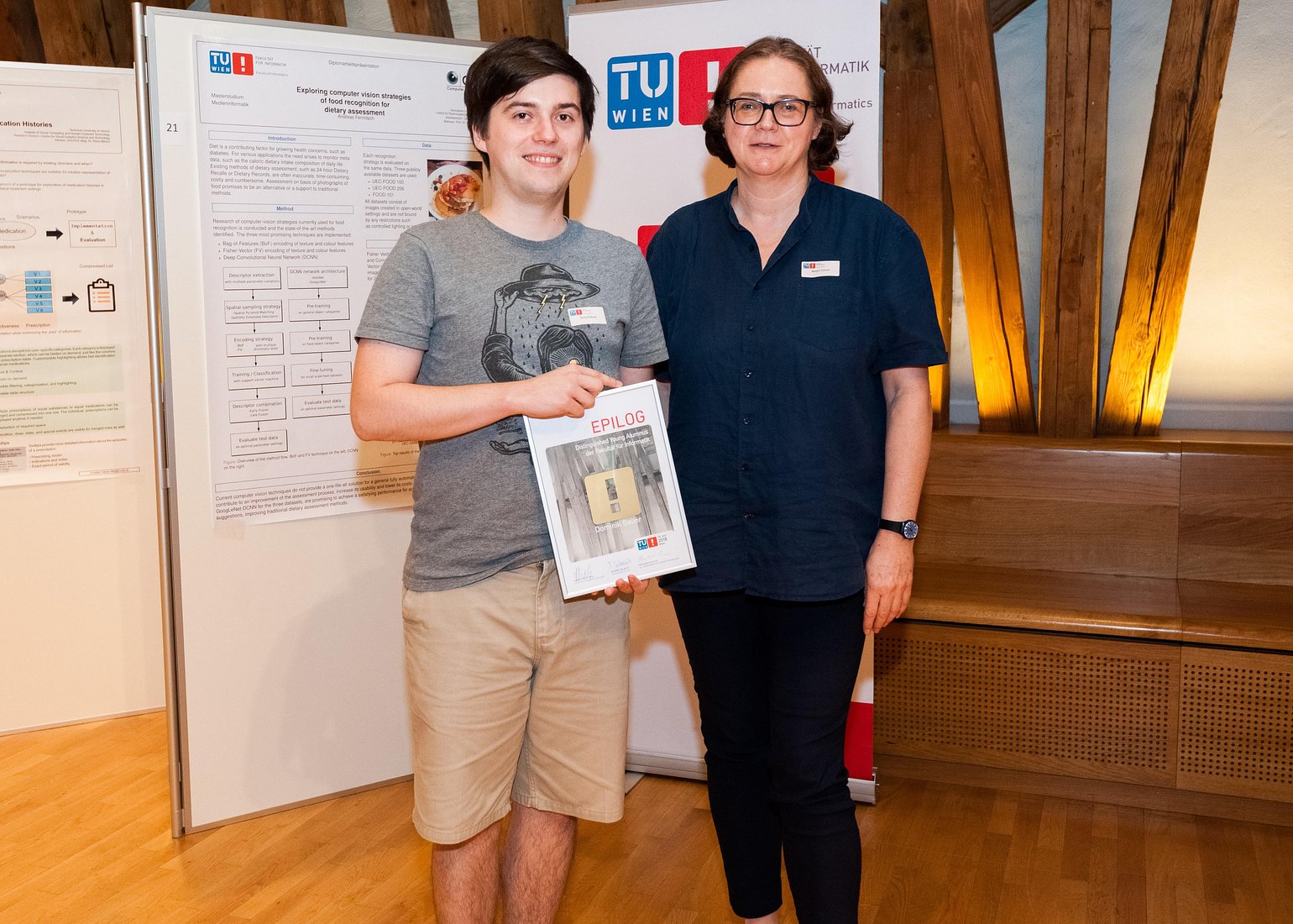 Prof. Dr. Margrit Gelautz, Vorsitzende der EPILOG-Jury, übergibt den Hauptpreis an Dominik Bauer für seine Diplomarbeit "Evaluation of the Recognition Distances of Safety Signs in VR Considering Vision Impairments"